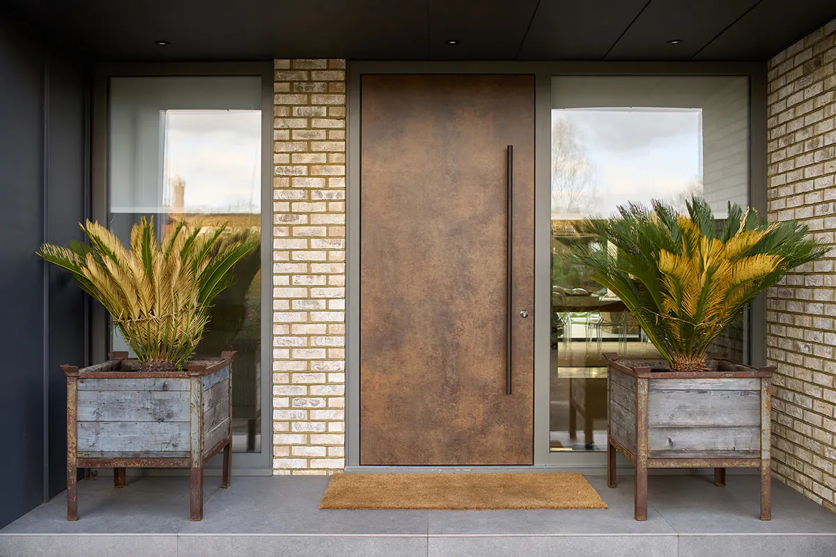 Modern home front with matching front and garage doors by Deuren. A slab style, the Olivio door has a warm patina bronze, metallic finish.