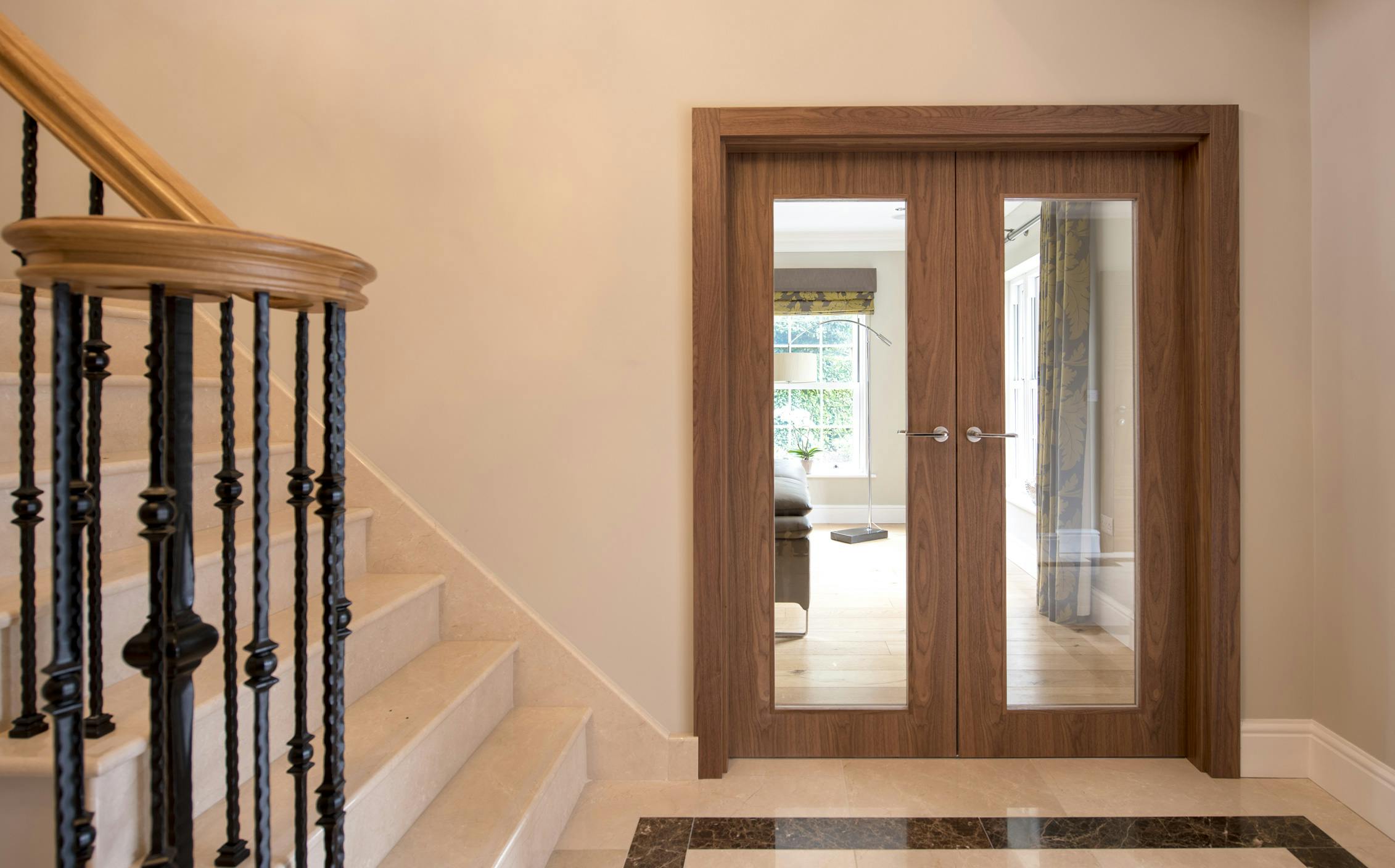 Luxurious hallway with side view of iron staircase and bespoke double door set by Deuren - Gio glass, Walnut finish, clear glass and chrome lever handles.