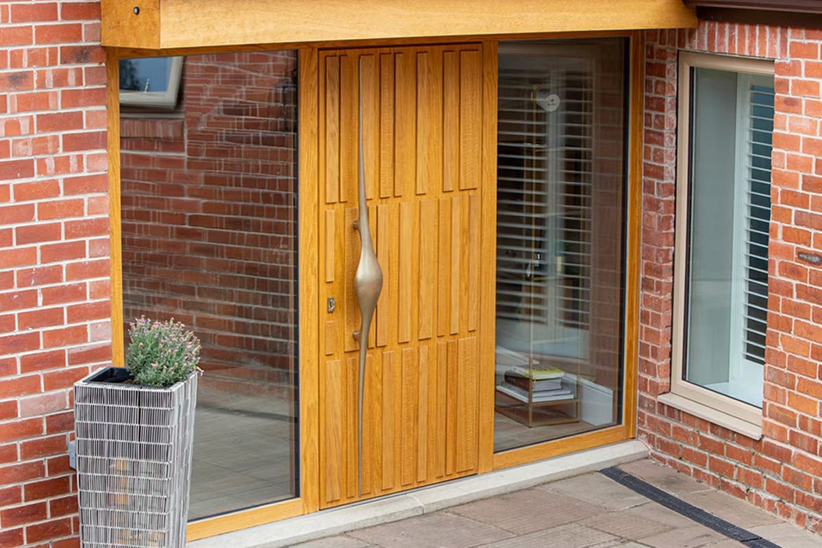 A bespoke Deuren front door design with irregular linear detail across three rows - Tavole, Honey Oak with long sculptural handle.