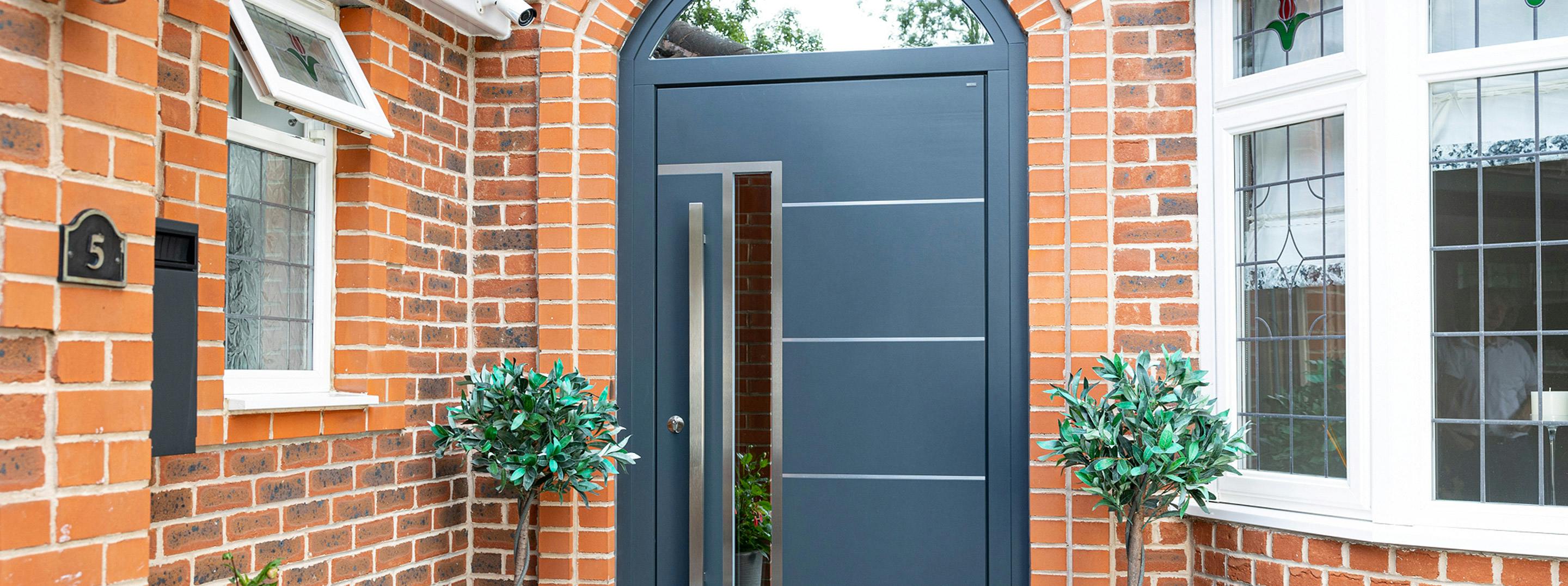 Modern front door made by Deuren - Pianura 2 style with a vertical glazed panel along side a long bar handle. Has 4 evenly spaced horizontal stainless steel inlays