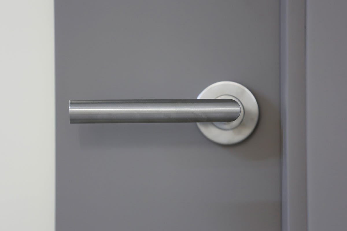 Close-up of stainless steel lever handle on a grey door.