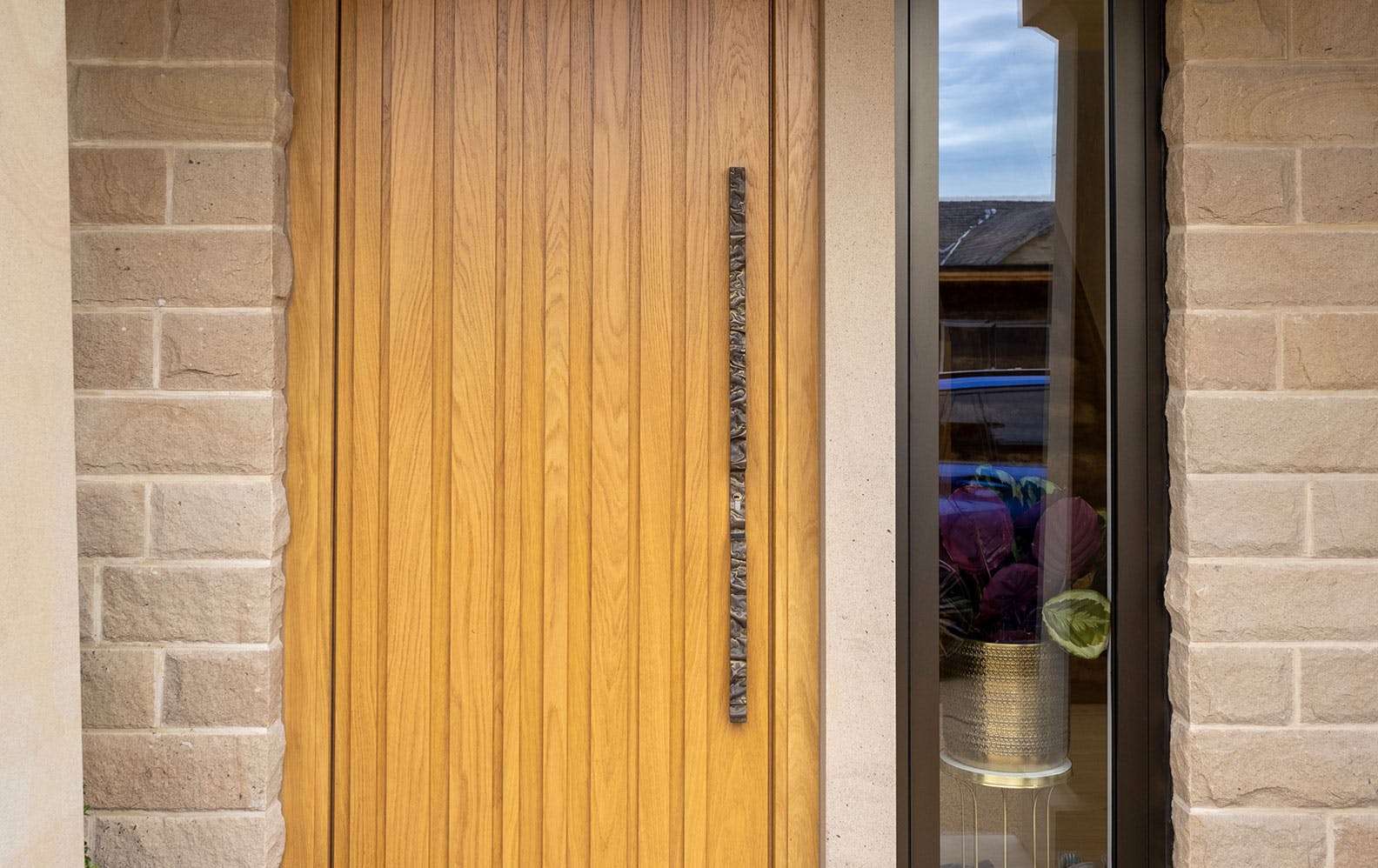 A close up of Deuren's Pianura front door design. It has irregular vertical strips that are raised and its finish is honey oak.