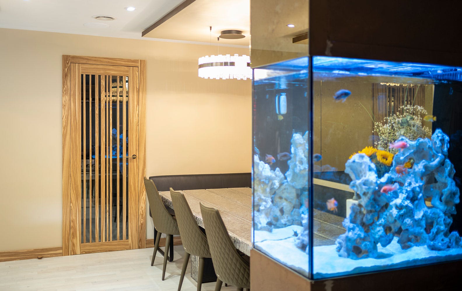 A modern dining area with tropical fish tank in the foreground. Features a bespoke Deuren, Gio glass doors with irregular vertical timber strips, in olive oak.