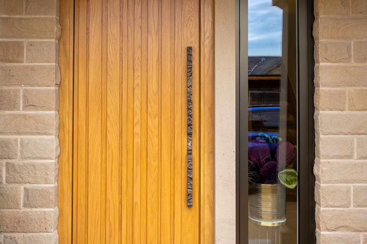 A close up of Deuren's Pianura front door design. It has irregular vertical strips that are raised and its finish is honey oak.