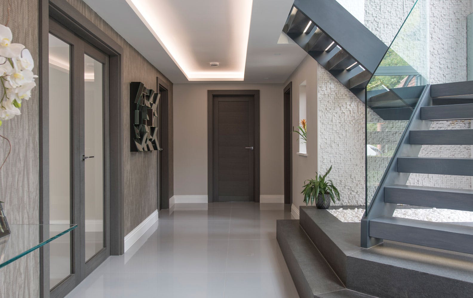 A contemporary hallway and staircase with a combination of double and single door sets, and solid and glazed Gio door designs by Deuren, all finished in Grey Oak to harmonise with the grey interior.