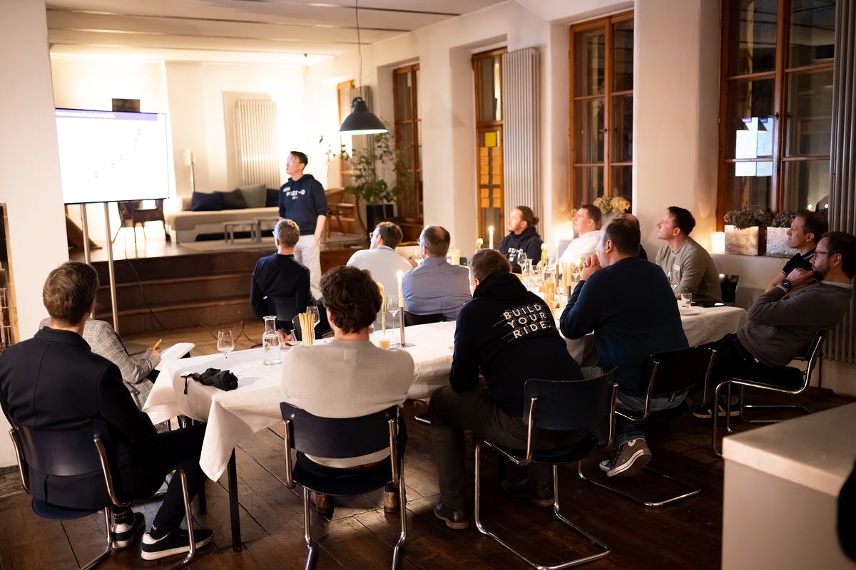 Gruppenfoto vom Tech Lead Roundtable von DevBoost in Dresden: Mehrere technische Führungskräfte aus Softwareunternehmen sitzen gemeinsam an einem Tisch und verfolgen eine Präsentation über Softwareentwicklung und Skalierung. Im Vordergrund: entspannter Austausch auf Augenhöhe in wohnlicher Atmosphäre.
