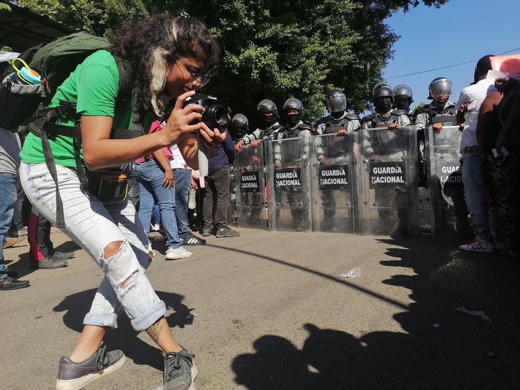 reportera toma fotografias con su camara, al fondo se ven elementos de la guardia nacional