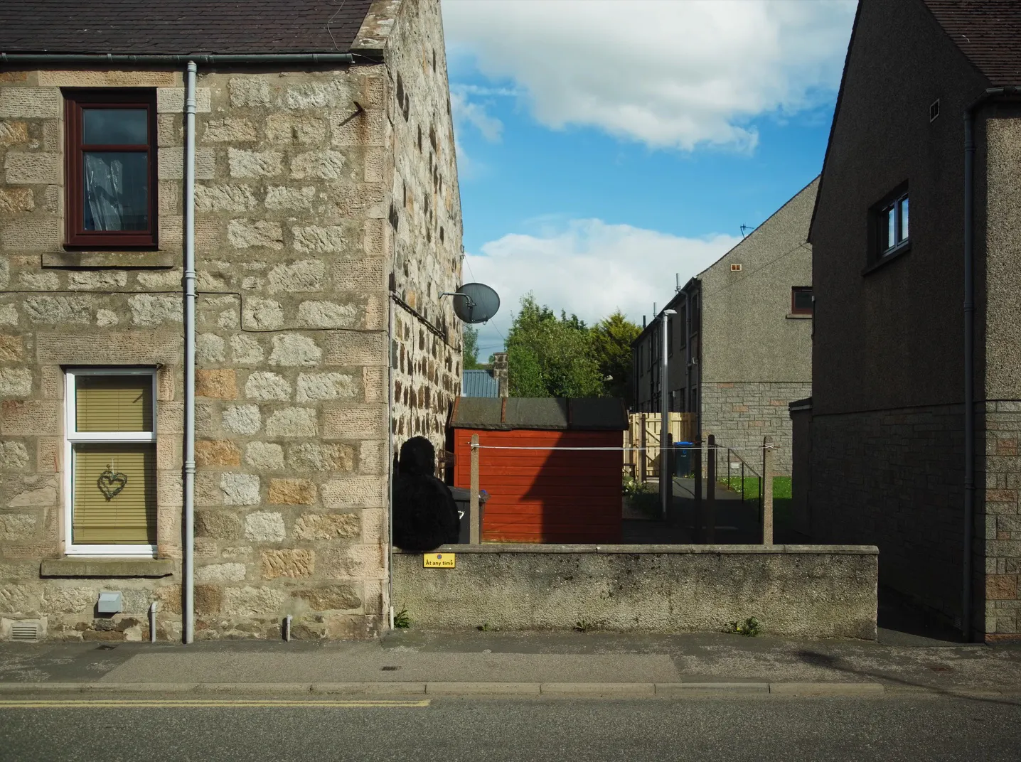 A film still showing a black hairy monster sat on a wall between stone houses.