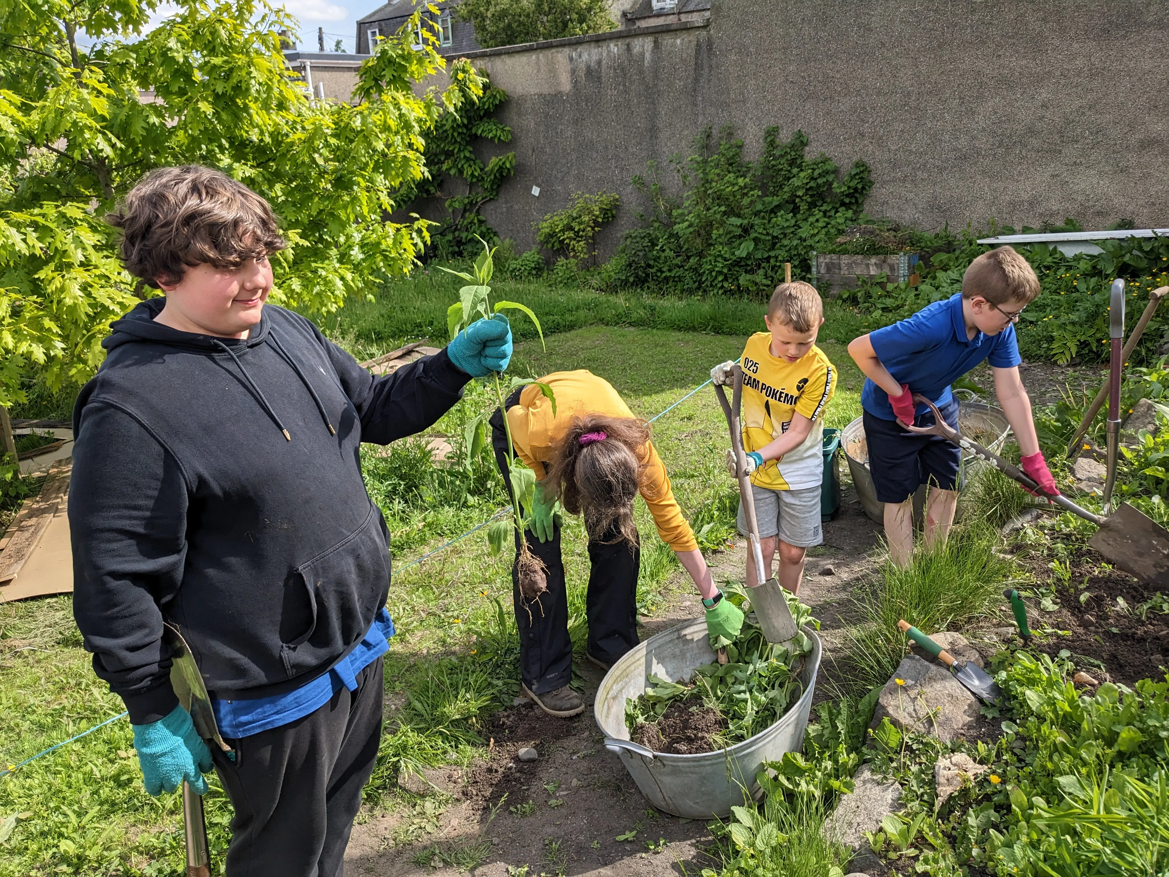 A group of children and adults are preparing a hole for a pond in the Brander Community Garden