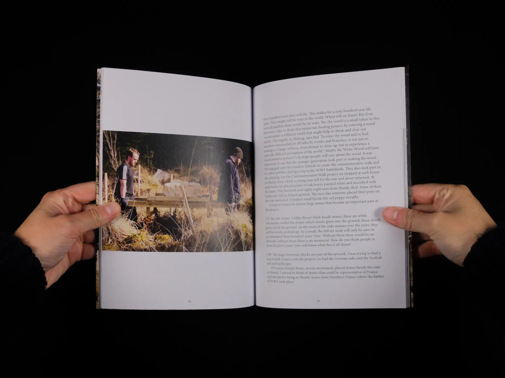 A double page spread: on the left, two people carry a boulder through long grass, with text on the right hand page 