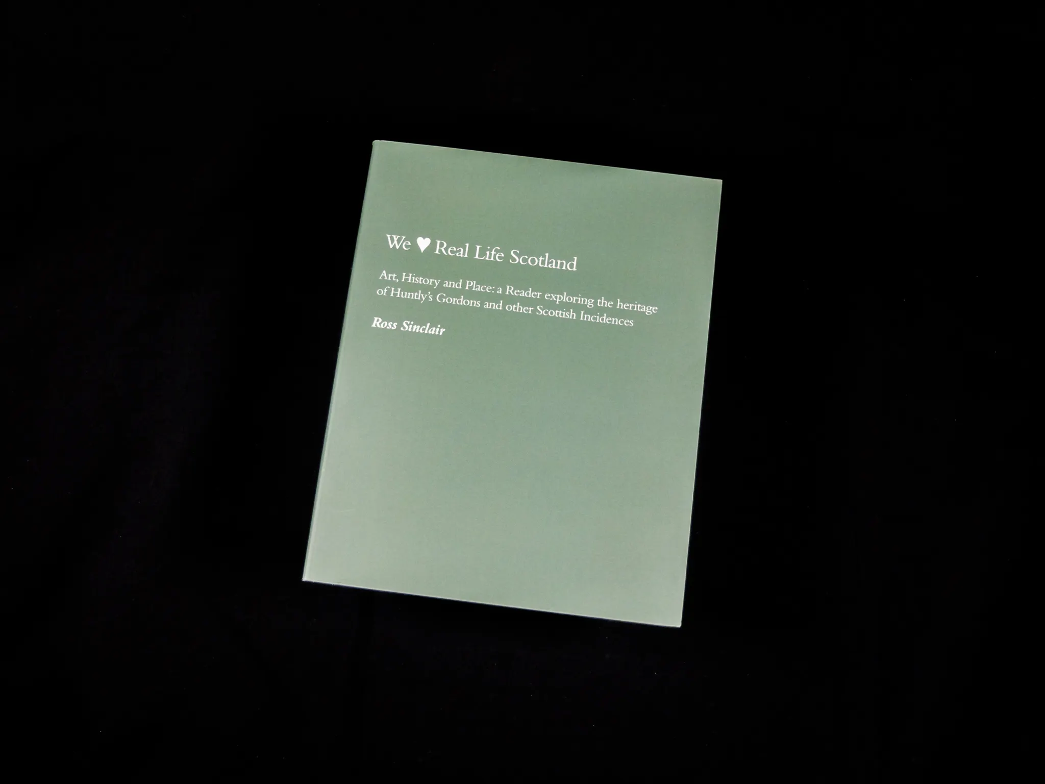 A book with a dark green cover on a black background. The top half of the book features the title in white text. 