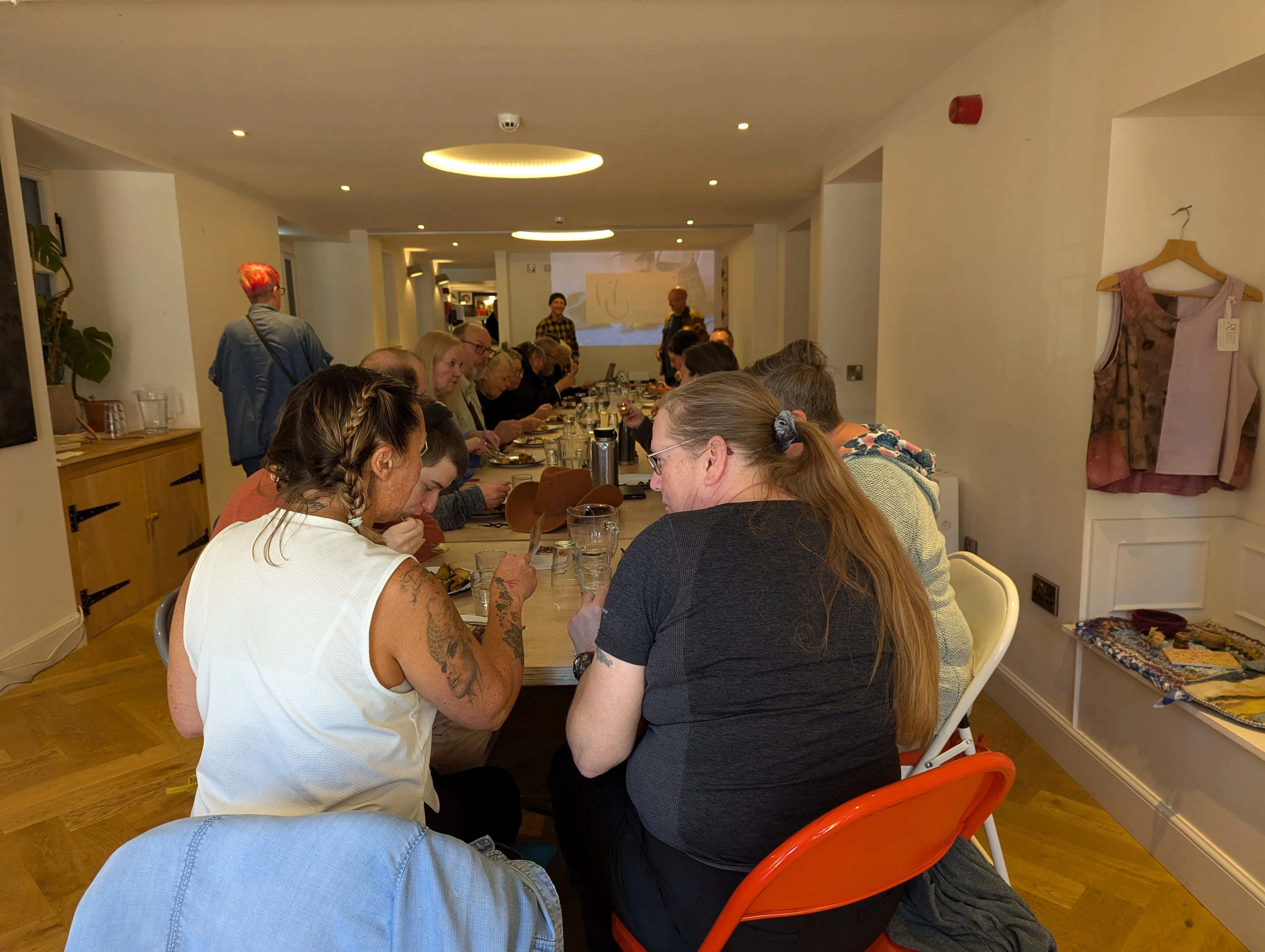 A photo showing people sitting eating at a long table in a white room.