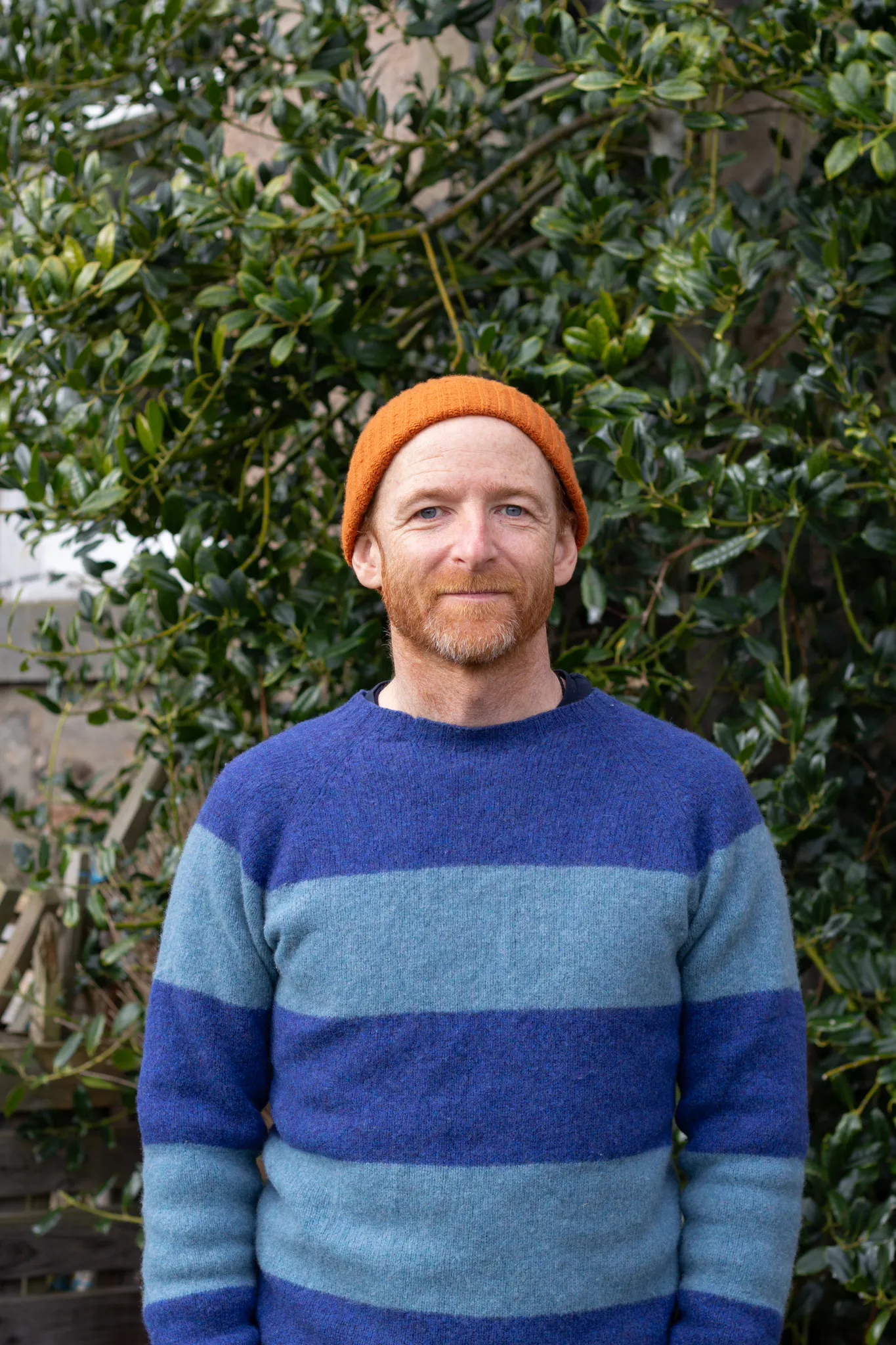 Bruce is a light-skinned, freckled man with ginger stubble. He is wearing an orange beanie hat and blue stripey jumper.
