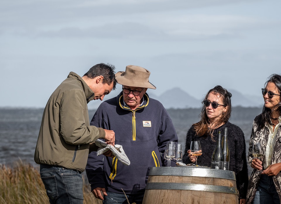 People gathered around a wine barrel next to Moulting Lagood with the backdrop of Hazards Mountain Range