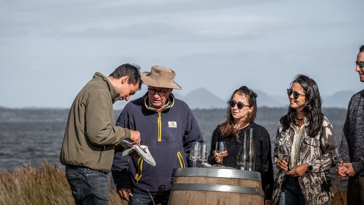 People gathered around a wine barrel next to Moulting Lagood with the backdrop of Hazards Mountain Range
