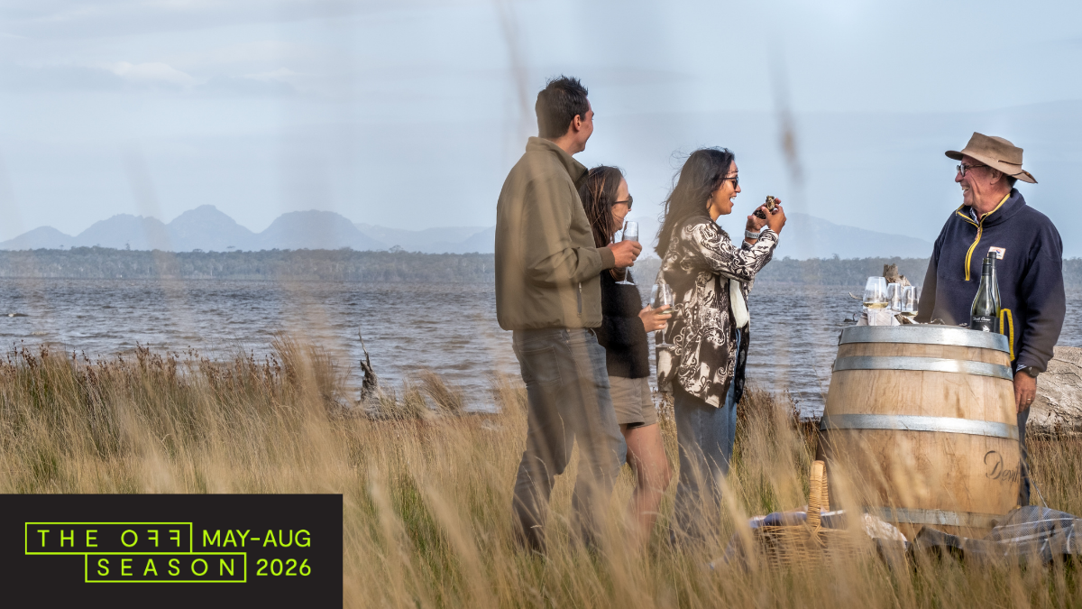 People gathered around a wine barrel next to Moulting Lagoon with the backdrop of Hazards Mountain Range