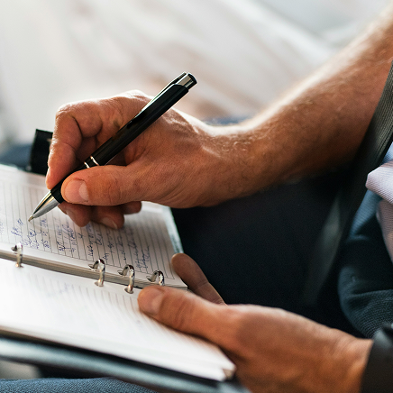 Close-up of a person writing in an open planner with a black pen.