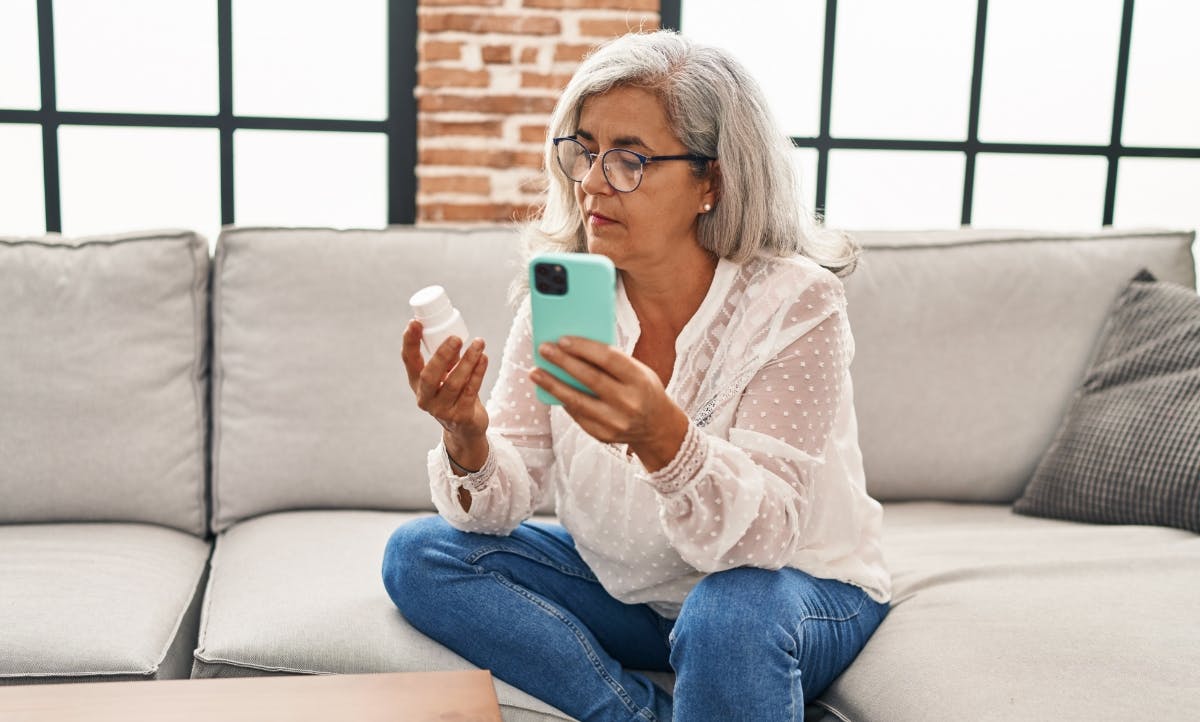 A female member sitting on couch reviewing her prescription with her mobile phone.