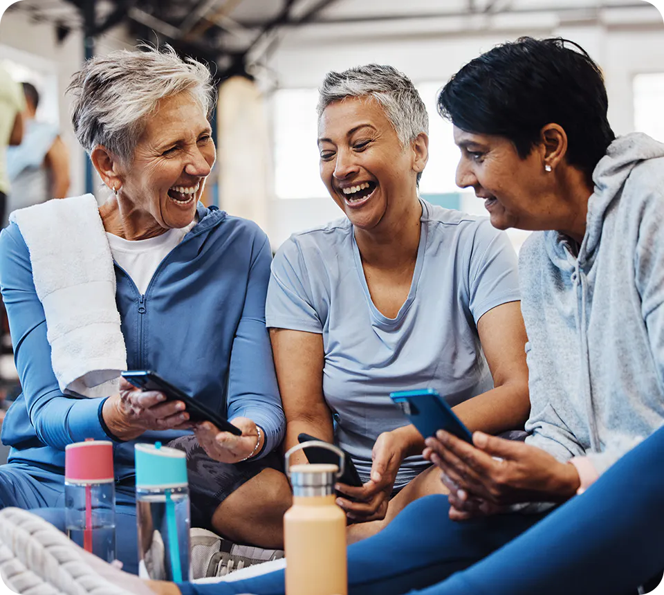 Three women in athletic wear sitting together, laughing while looking at smartphones.