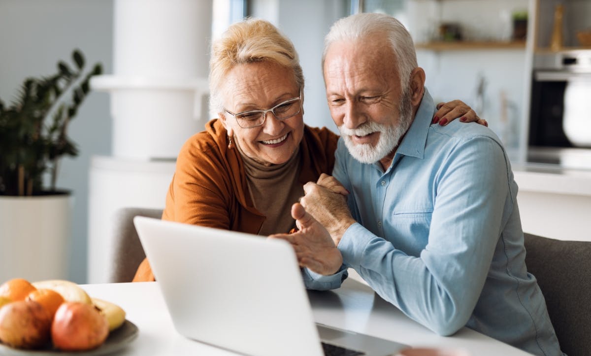 A happy older couple browsing the Internet together on a laptop at home.