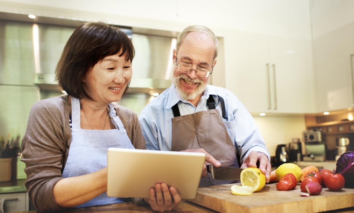 Husband and wife cooking while looking at recipe on a tablet.