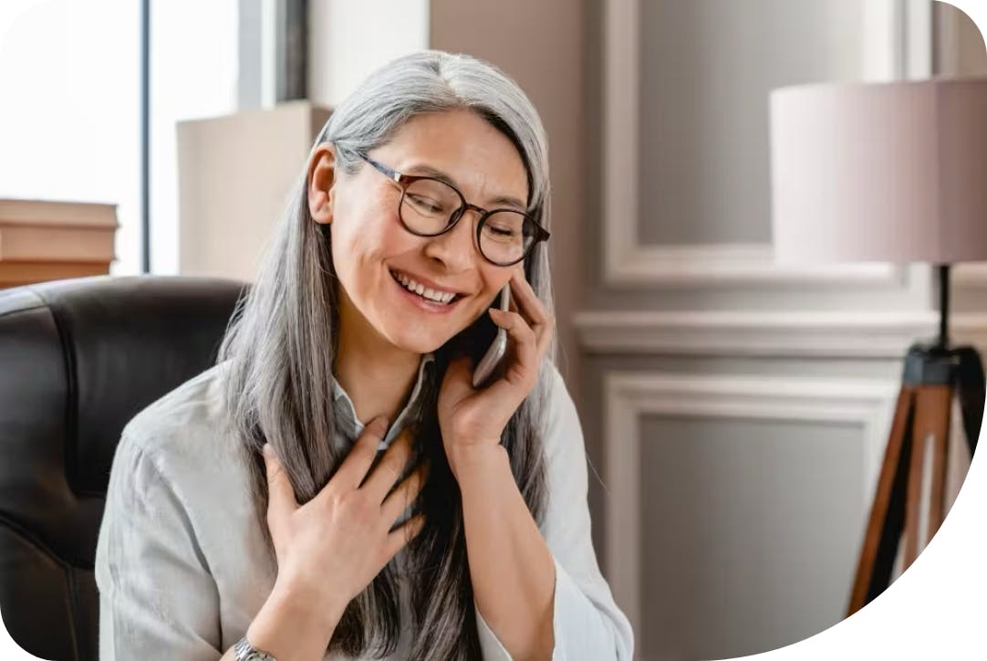 A woman with glasses and a white shirt is speaking on a mobile phone.
