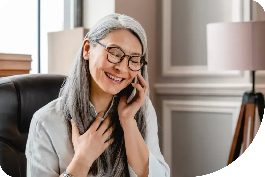A woman with glasses and a white shirt is speaking on a mobile phone.
