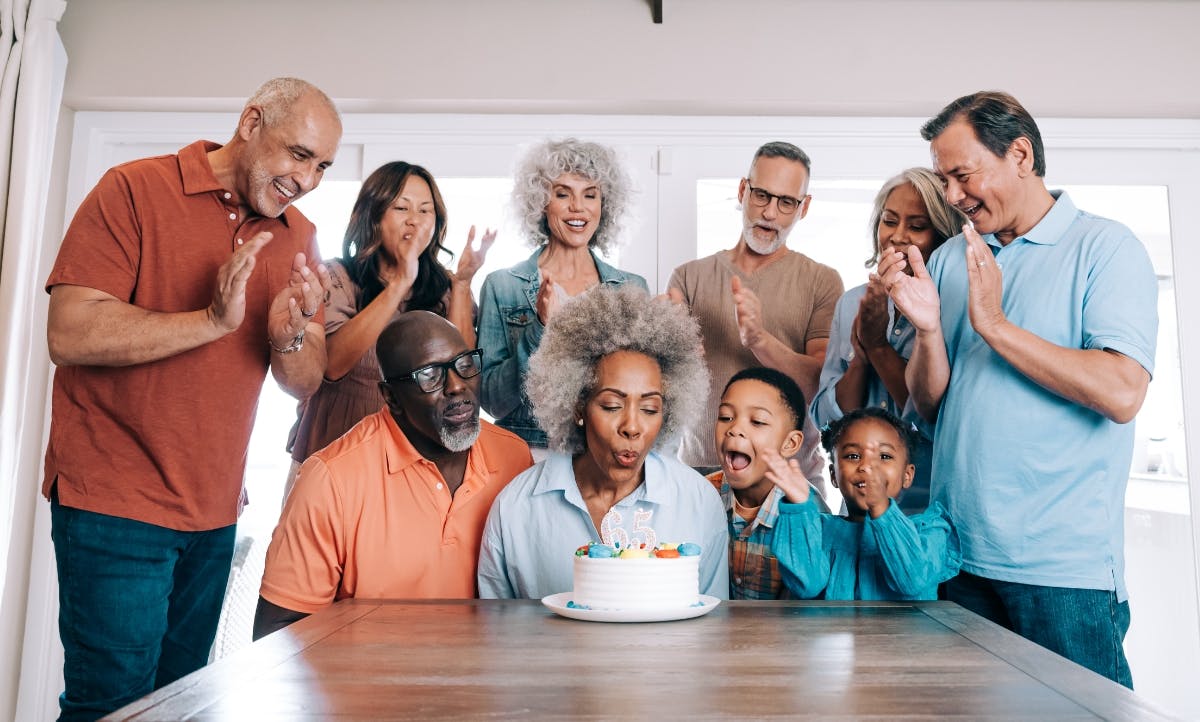 A joyful gathering of friends and family, celebrating a 65th birthday with smiles, laughter, and a delicious cake on the table.