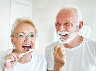 A Devoted Health couple brushing their teeth in front of a bathroom mirror.