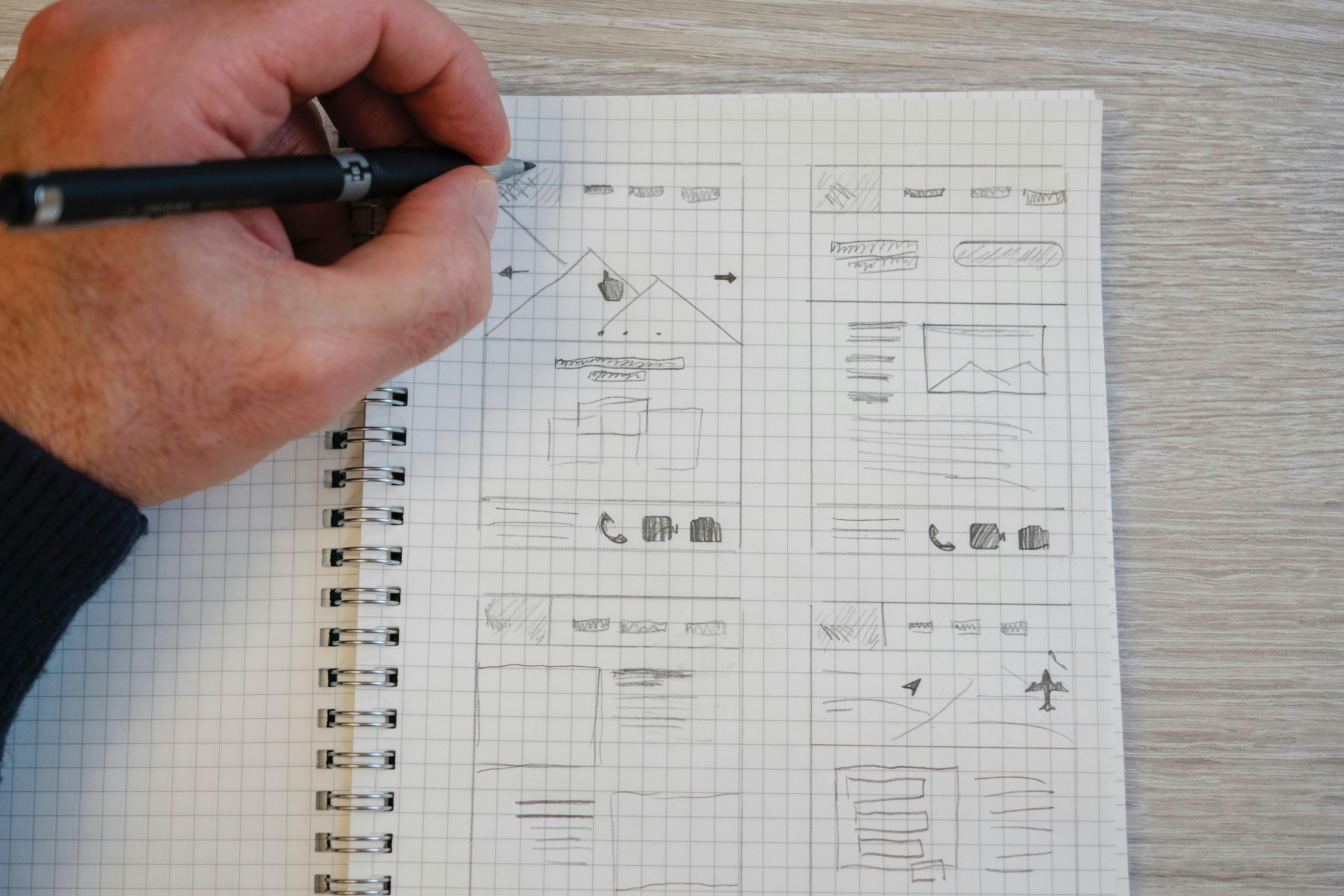 Männliche Hand zeichnet Wireframes in ein Notitzbuch