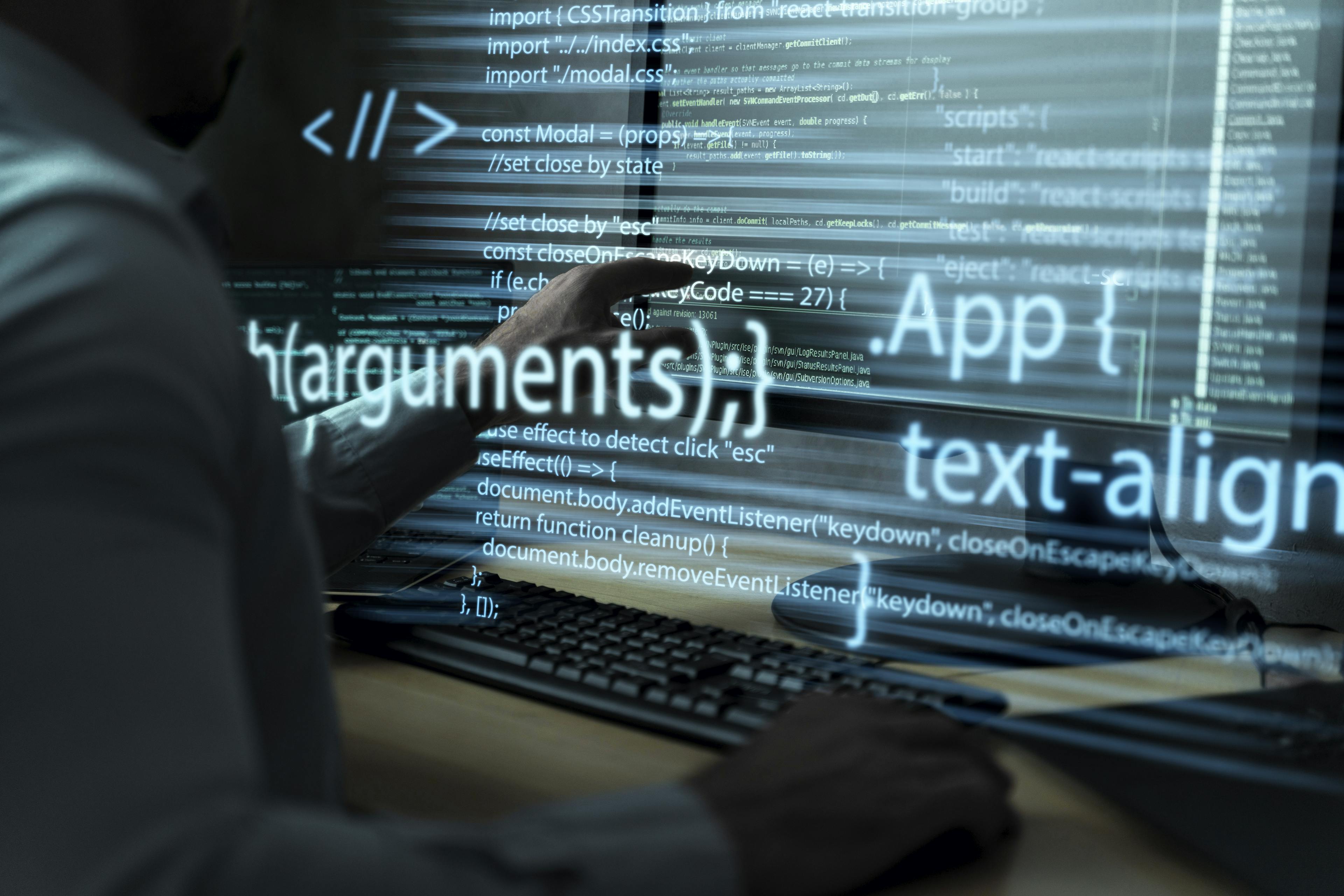 Closeup of hands typing on a keyboard with overlay of code and programming terms on the screen.