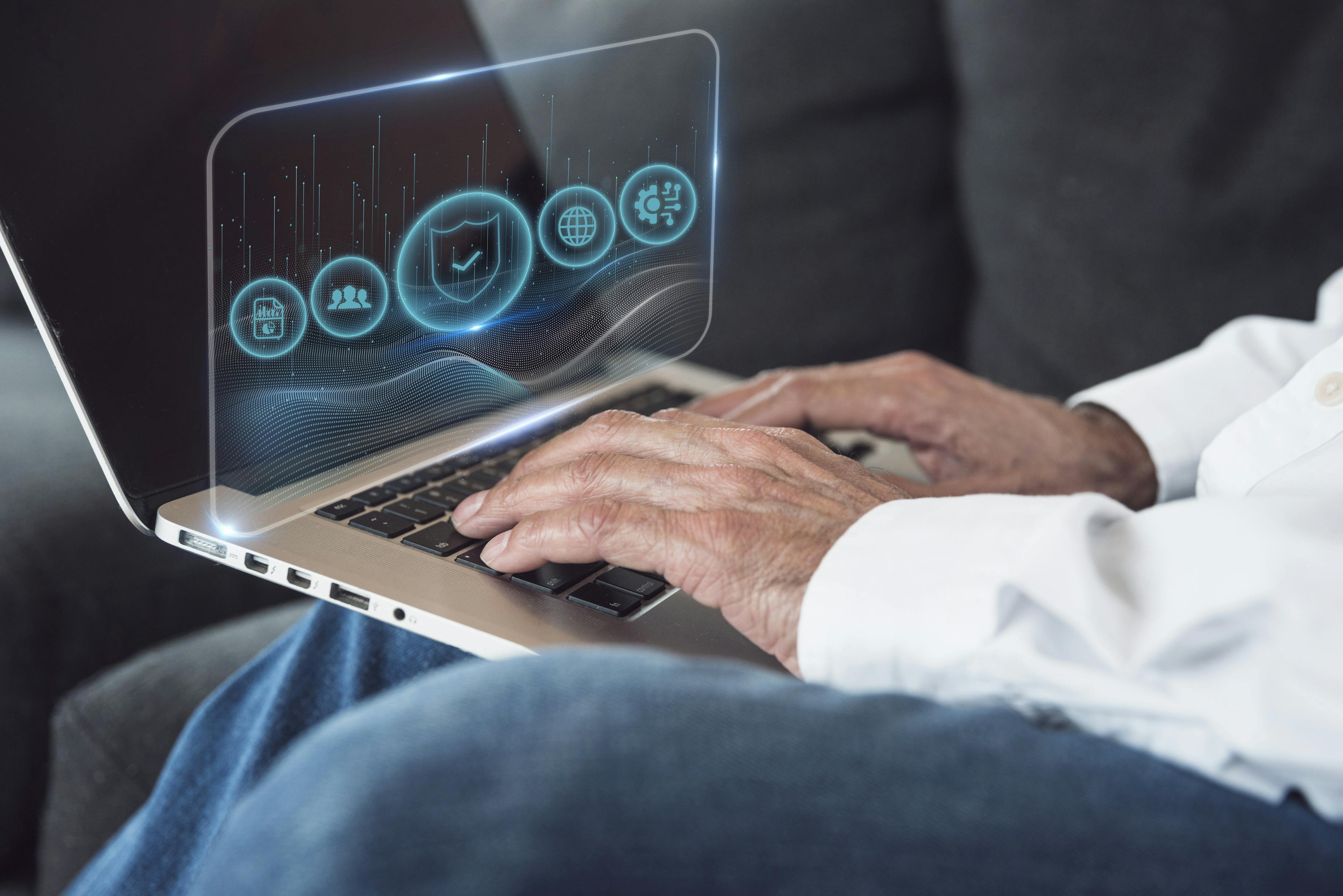 Closeup of a person typing on a laptop with holographic digital icons displayed above the keyboard.