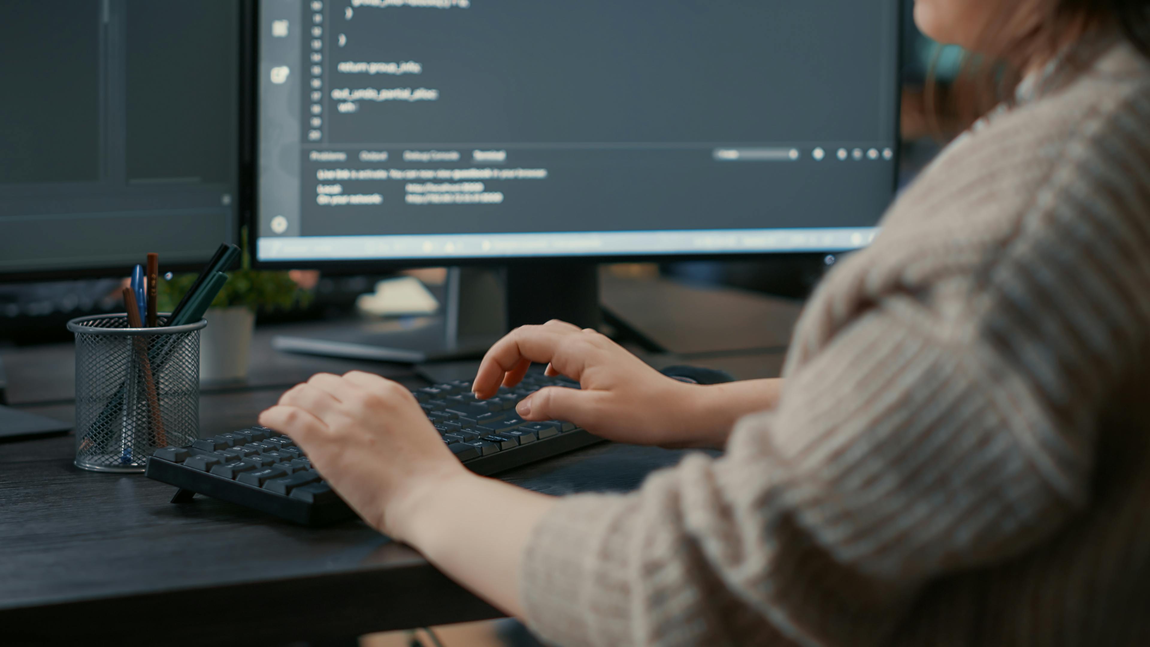 Closeup of a programmer's hands typing on a keyboard with code on a computer monitor