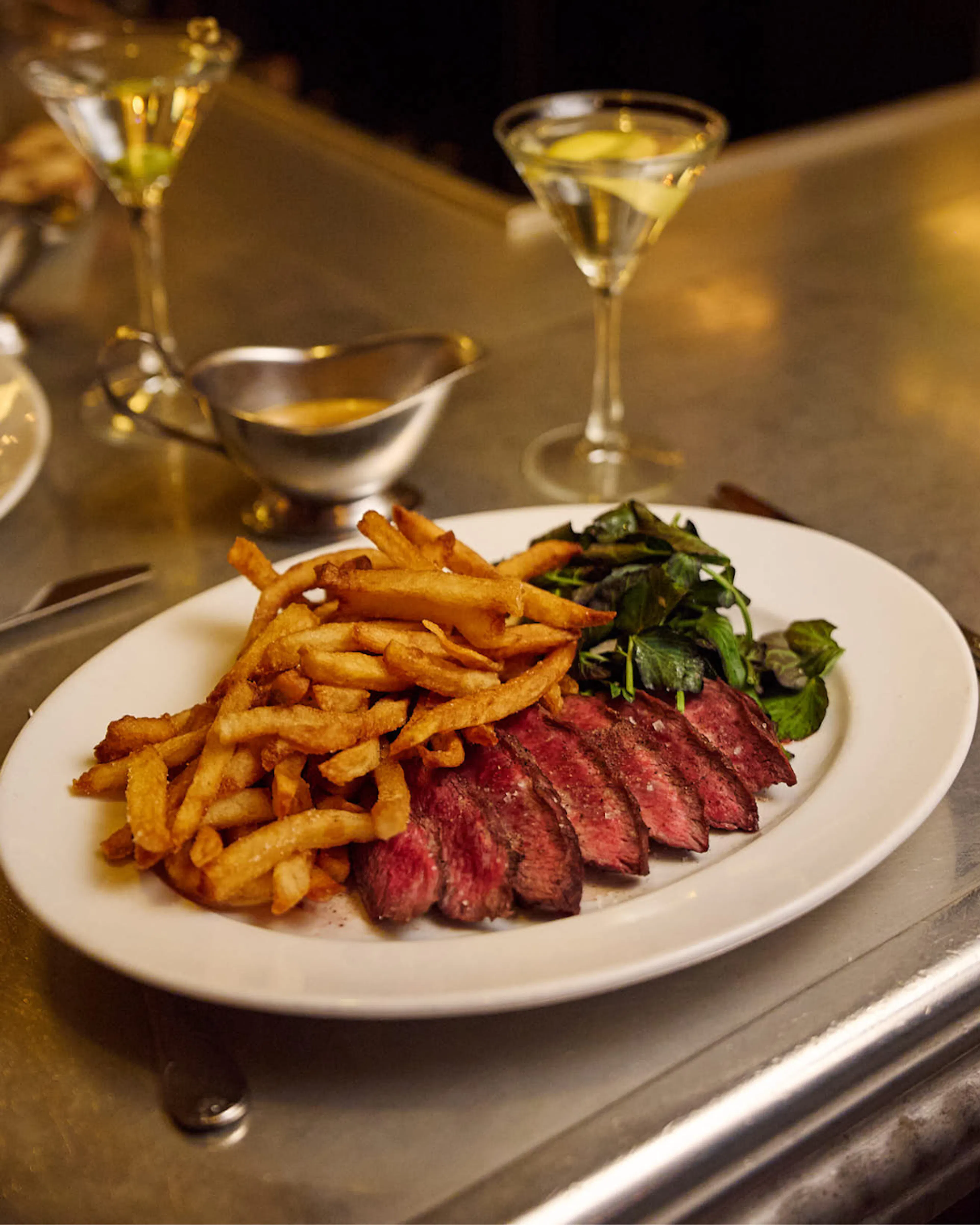 Steak-frites à l’échalote at Le Gratin, featuring grilled Prime Black Angus flatiron steak with red wine-shallot sauce, French fries, and watercress salad.