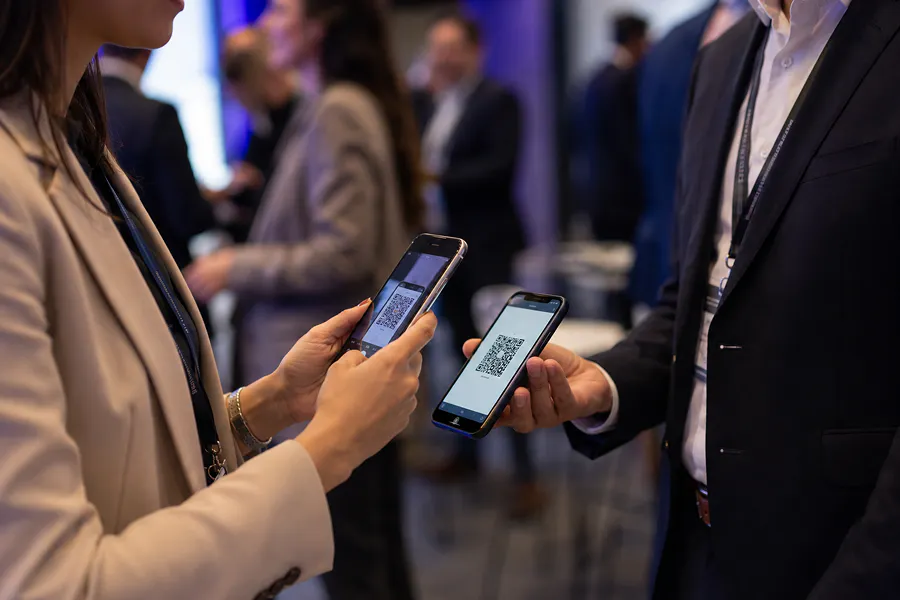 Close-up of two attendees scanning each other's QR code displayed on their smartphones, illustrating a digital contact exchange at a professional event.