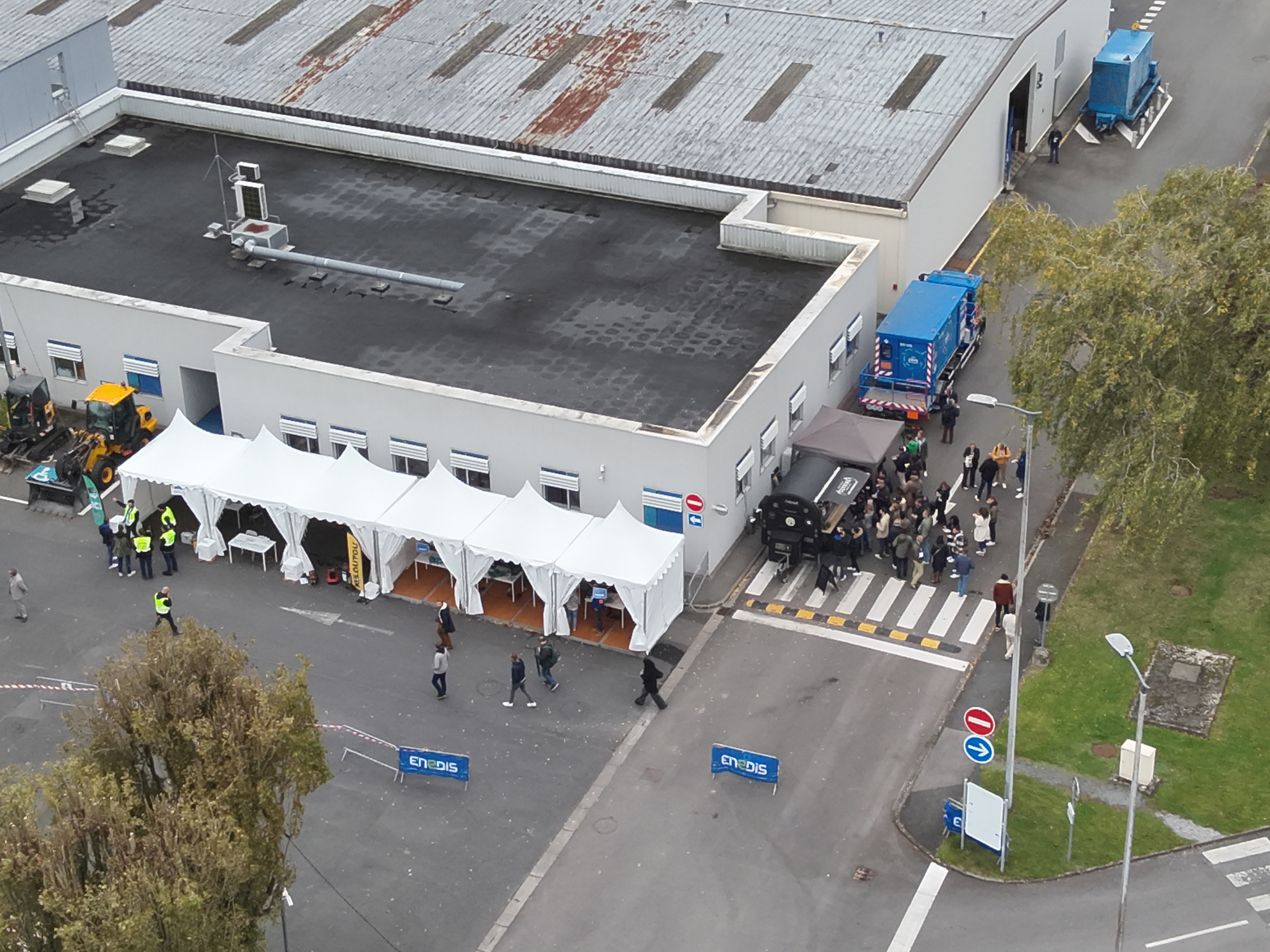 Vue aérienne d'un forum Enedis avec des tentes blanches alignées pour l'accueil des participants, des équipes en gilets de sécurité, et une zone extérieure aménagée pour les visiteurs, illustrant une logistique événementielle efficace.