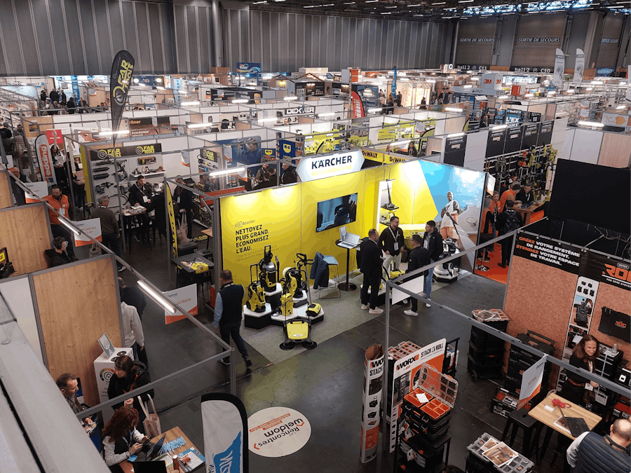 Vue aérienne d'un salon professionnel avec de nombreux stands d'exposants, dont Kärcher et d'autres marques du secteur industriel et de l'outillage. Les visiteurs échangent avec les exposants, explorent les produits exposés et circulent dans les allées du salon.