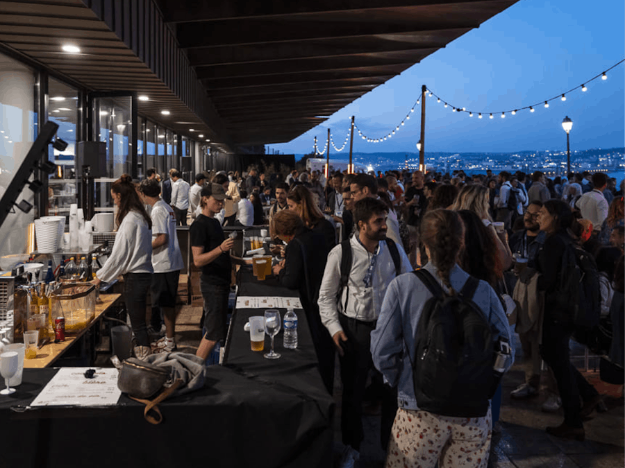 Soirée networking de la French Tech Aix-Marseille avec de nombreux participants réunis en extérieur sur une terrasse animée, ambiance conviviale avec bar, guirlandes lumineuses et vue sur la ville au crépuscule.