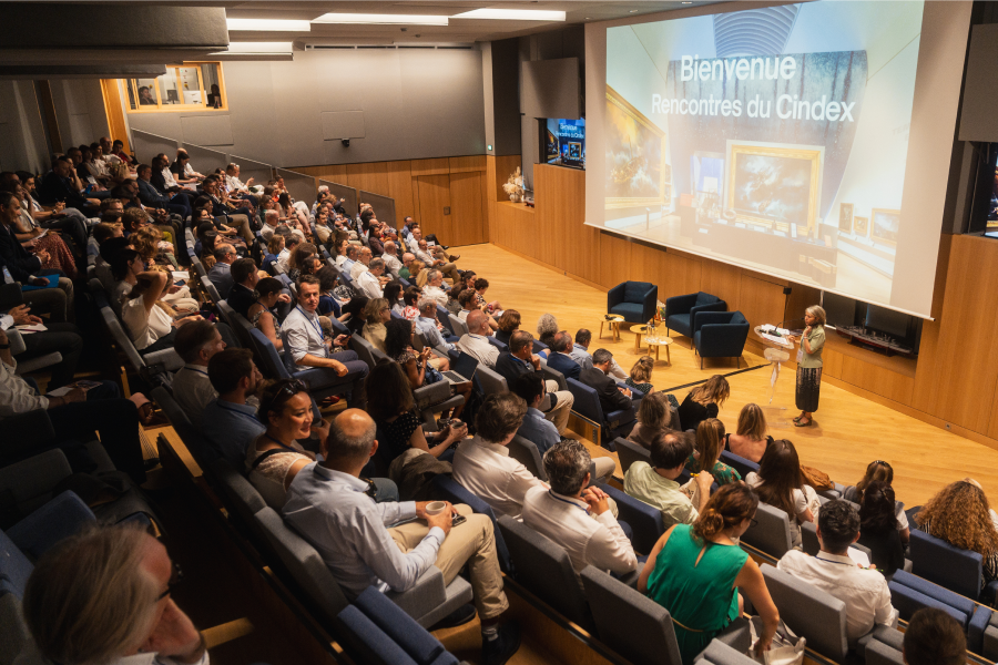 Auditorium rempli de participants assistant aux Rencontres du CINDEX, avec une intervenante sur scène devant un grand écran affichant « Bienvenue Rencontres du Cindex ».