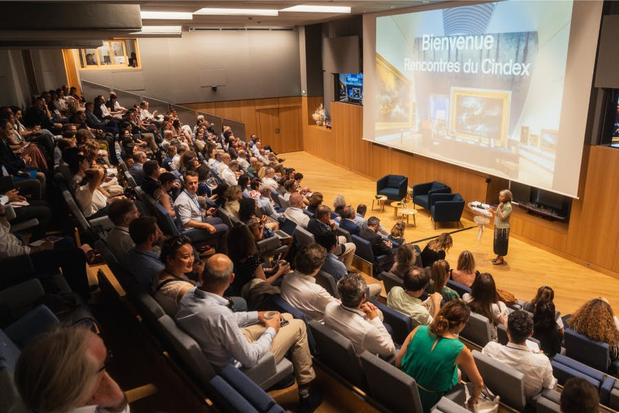 Auditorium rempli de participants assistant aux Rencontres du CINDEX, avec une intervenante sur scène devant un grand écran affichant « Bienvenue Rencontres du Cindex ».