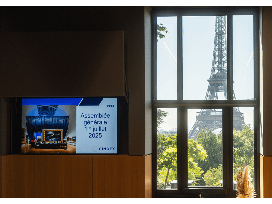 Écran annonçant l’assemblée générale CINDEX du 1er juillet 2025 avec vue sur la tour Eiffel à travers une fenêtre.