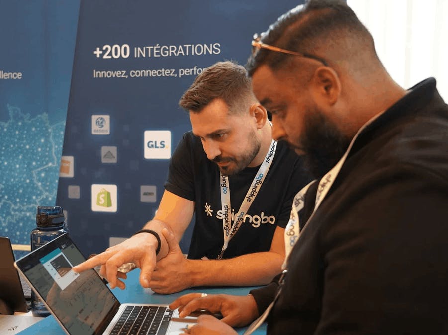 Dois profissionais a analisar um computador portátil durante uma demonstração no stand da Shippingbo.