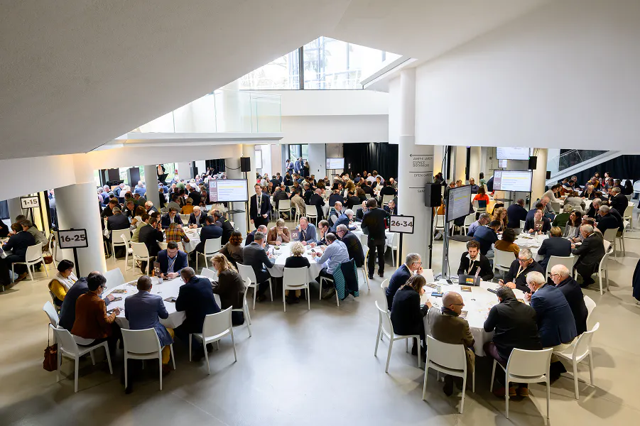 Business networking meetings with multiple roundtables and participants engaged in one-on-one discussions at a large-scale B2B congress