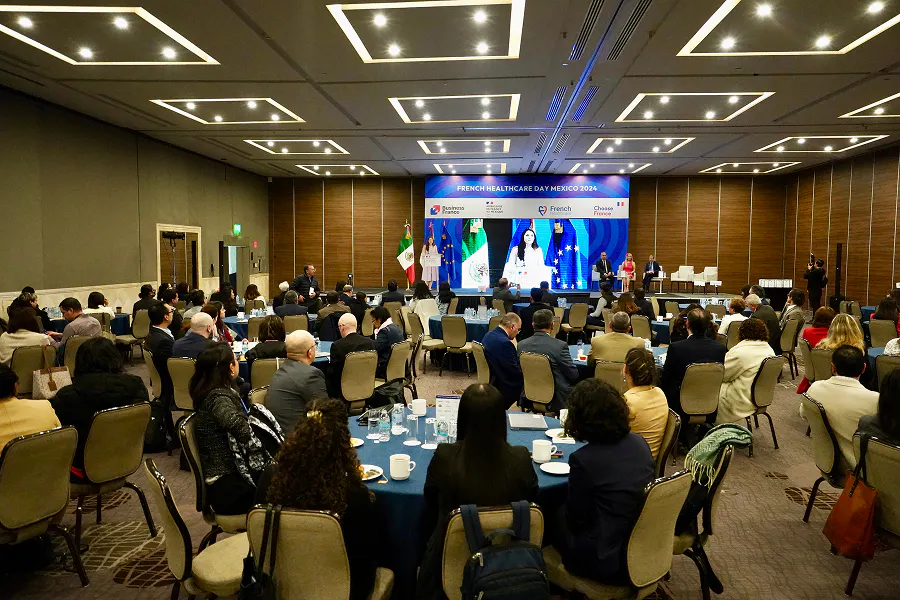 Attendees seated at round tables during the French Healthcare Day Mexico, watching a keynote session on stage with speakers and large screen presentation