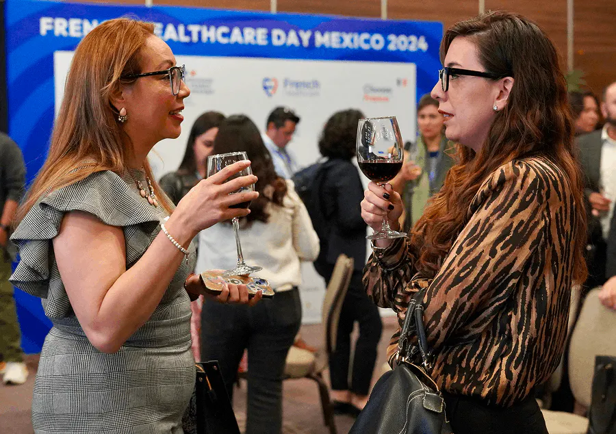 Two attendees chatting and networking over drinks during the French Healthcare Day Mexico, with other participants interacting in the background at a professional event