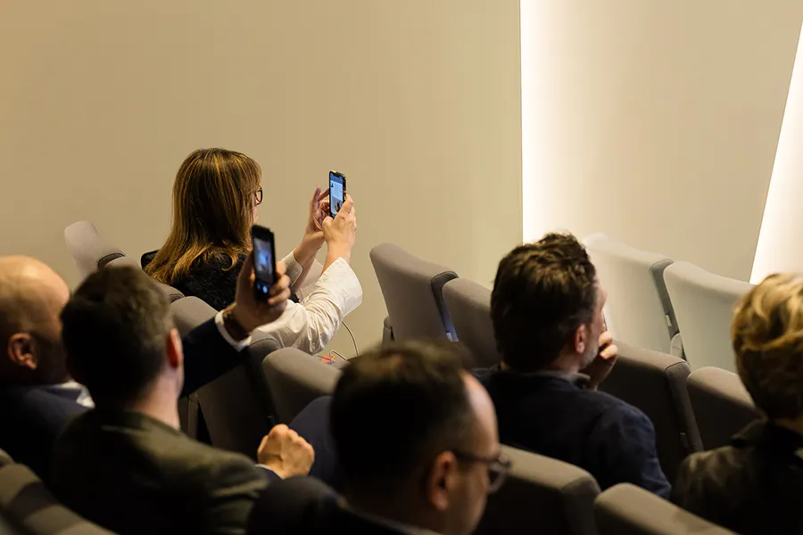 Participantes em auditório durante o Digital Habitat, utilizando smartphones para registrar e compartilhar momentos das conferências em um evento profissional focado em transformação digital.