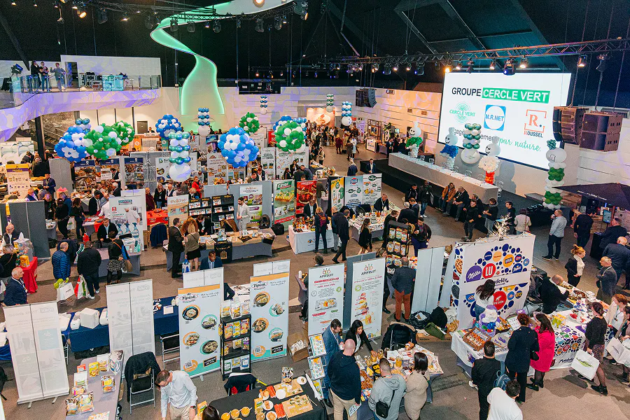 Aerial view of a large-scale B2B trade show: exhibitor booths, live networking, and hundreds of attendees on the show floor. From badge check-in to real-time attendance tracking : all managed from a single event management platform.
