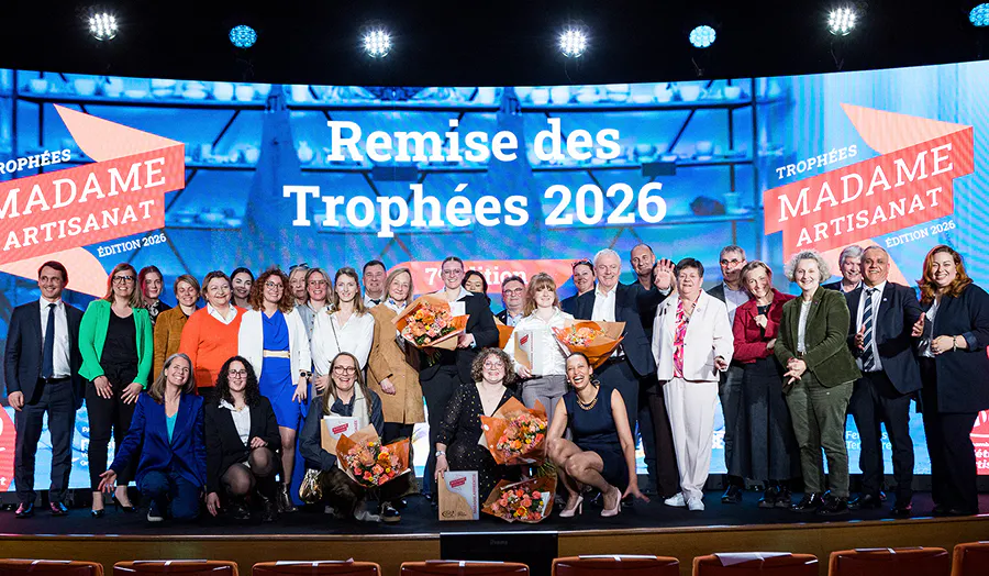 Photo de groupe sur scène réunissant les lauréates et intervenants d'une cérémonie de remise de trophées dédiée aux femmes artisanes. Plusieurs lauréates posent avec leur bouquet de fleurs, entourées de partenaires et personnalités, devant un écran géant affichant le nom de l'événement.