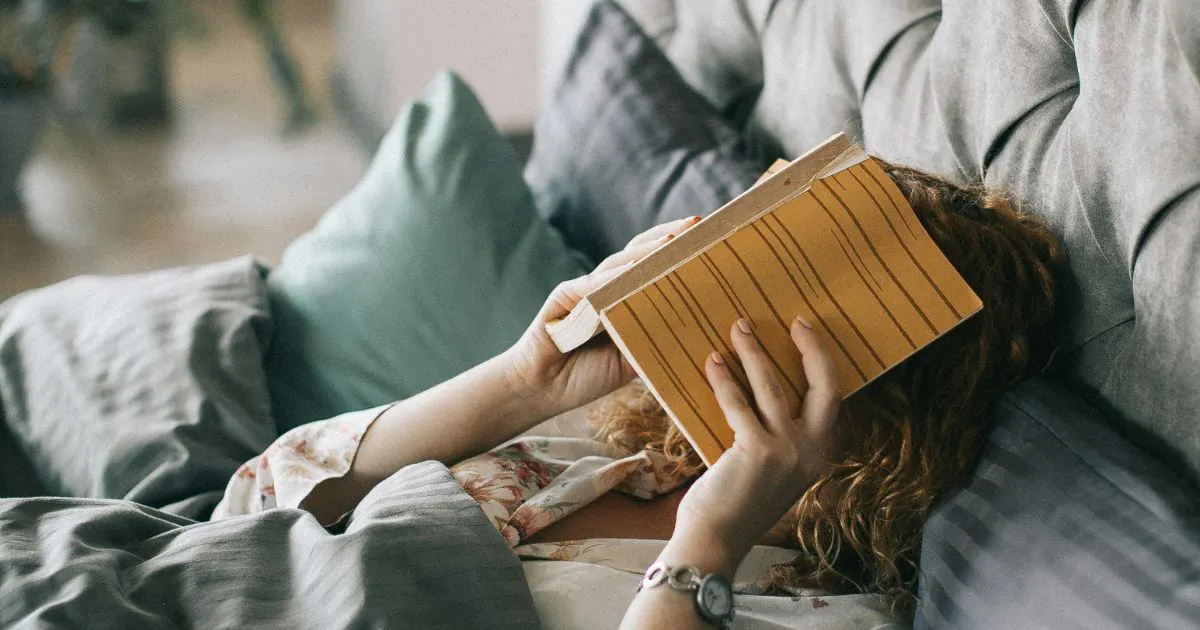 person lying on bed and covering face with a book