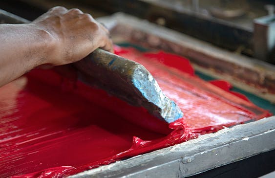 Pessoa passando tinta vermelha em uma tela da técnica de estamparia silk screen